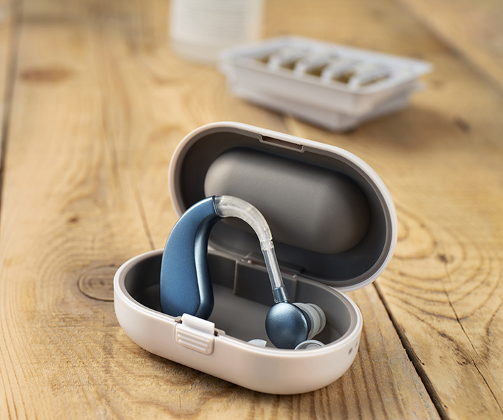 Audífono azul en su estuche de transporte sobre una mesa de madera.