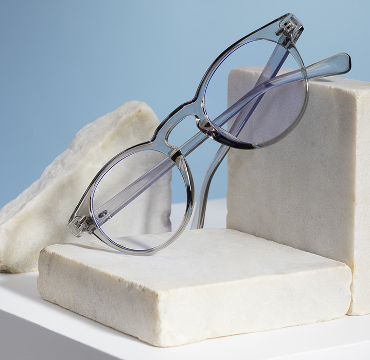 Gafas transparentes de montura redonda exhibidas sobre bloques de mármol.