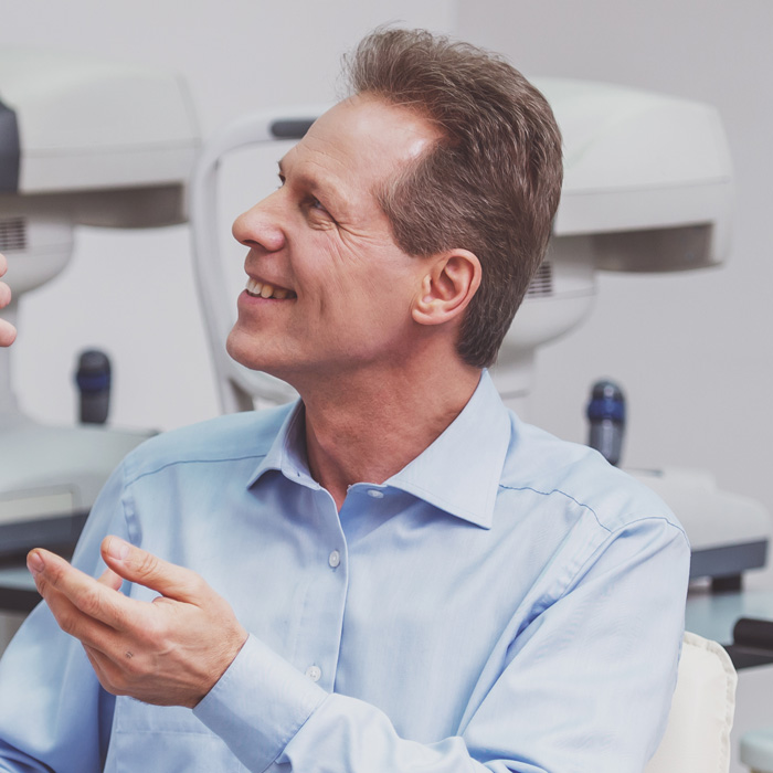 Hombre sonriendo e interactuando con el personal de la óptica, rodeado de equipos de examen visual.