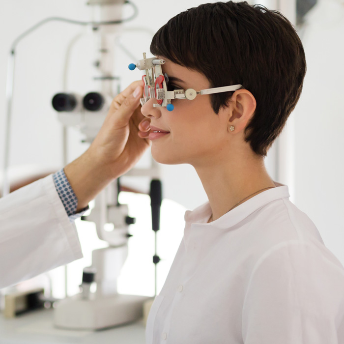 Especialista en óptica ajustando un foróptero a una paciente durante un examen de la vista.